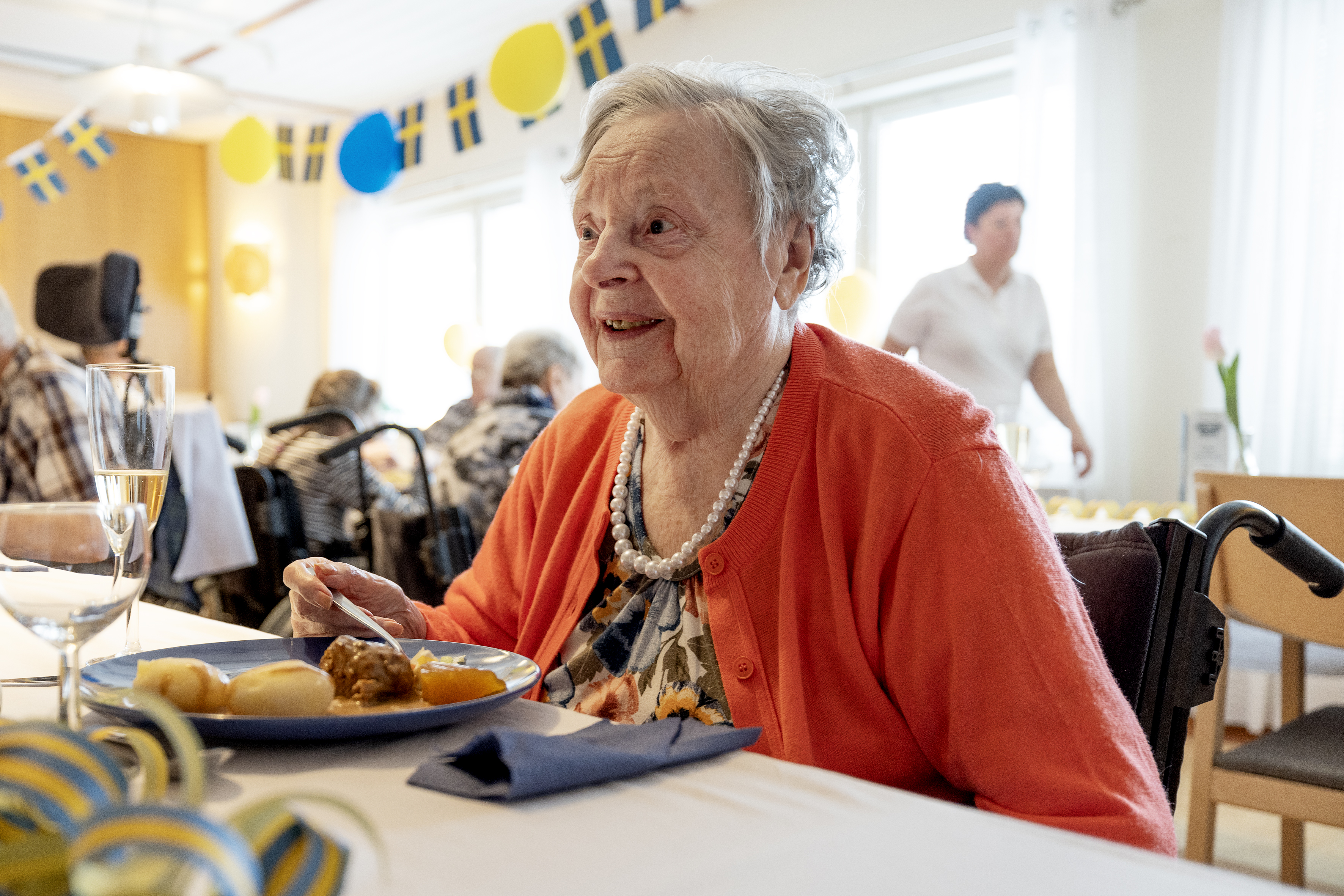En äldre person äter mat. Det är vimplar med svenska flaggan i bakgrunden.